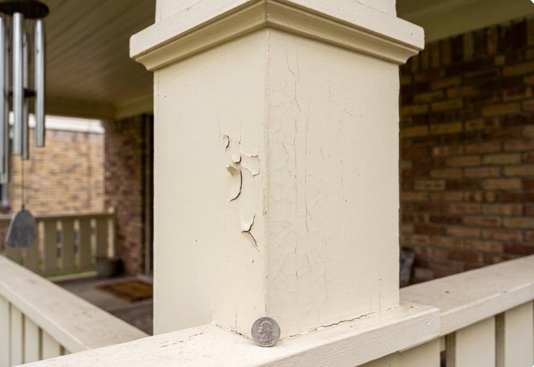 Cracked and lifting paint on a cream porch column, with a quarter for scale