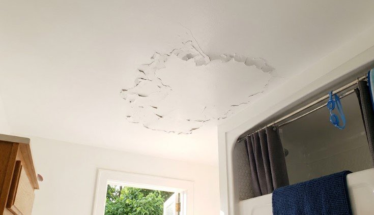 Small paint flakes clustered on a bathroom ceiling directly above the shower, caused by steam