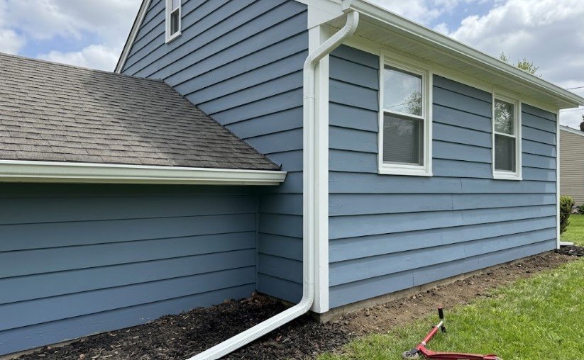 The same blue siding repainted, with a full-length downspout and extension carrying water away from the house