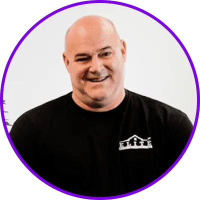 Bald man in a black shirt with a logo, smiling, framed in a purple circle.