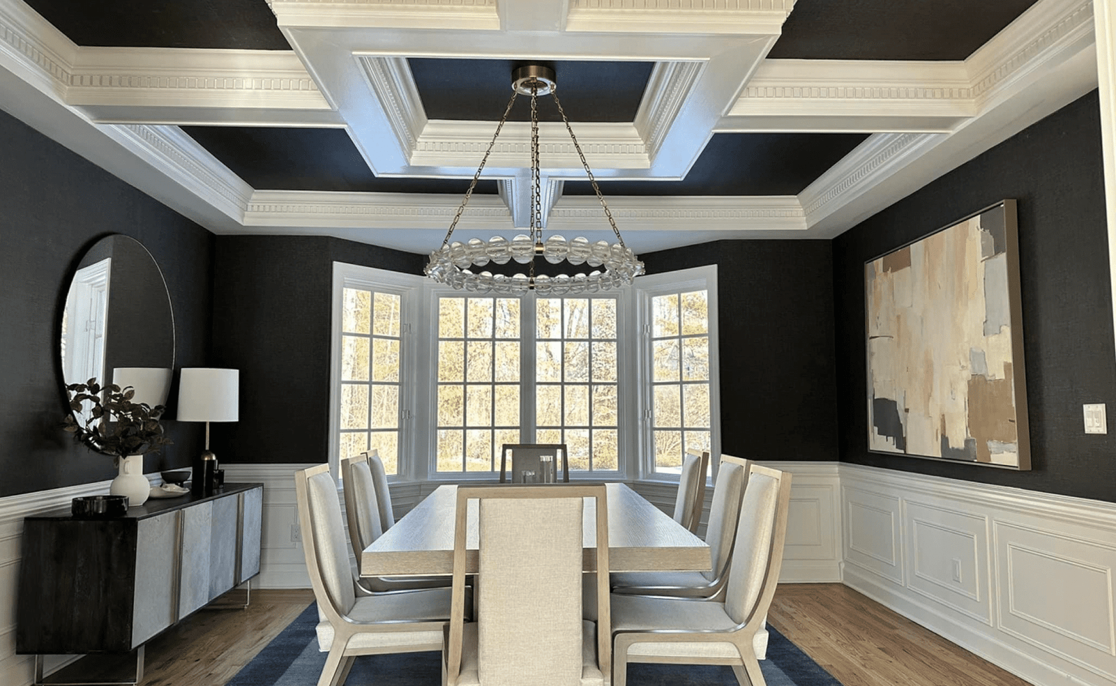 Dining room with table, eight chairs, coffered ceiling, large window, chandelier, art, sideboard.
