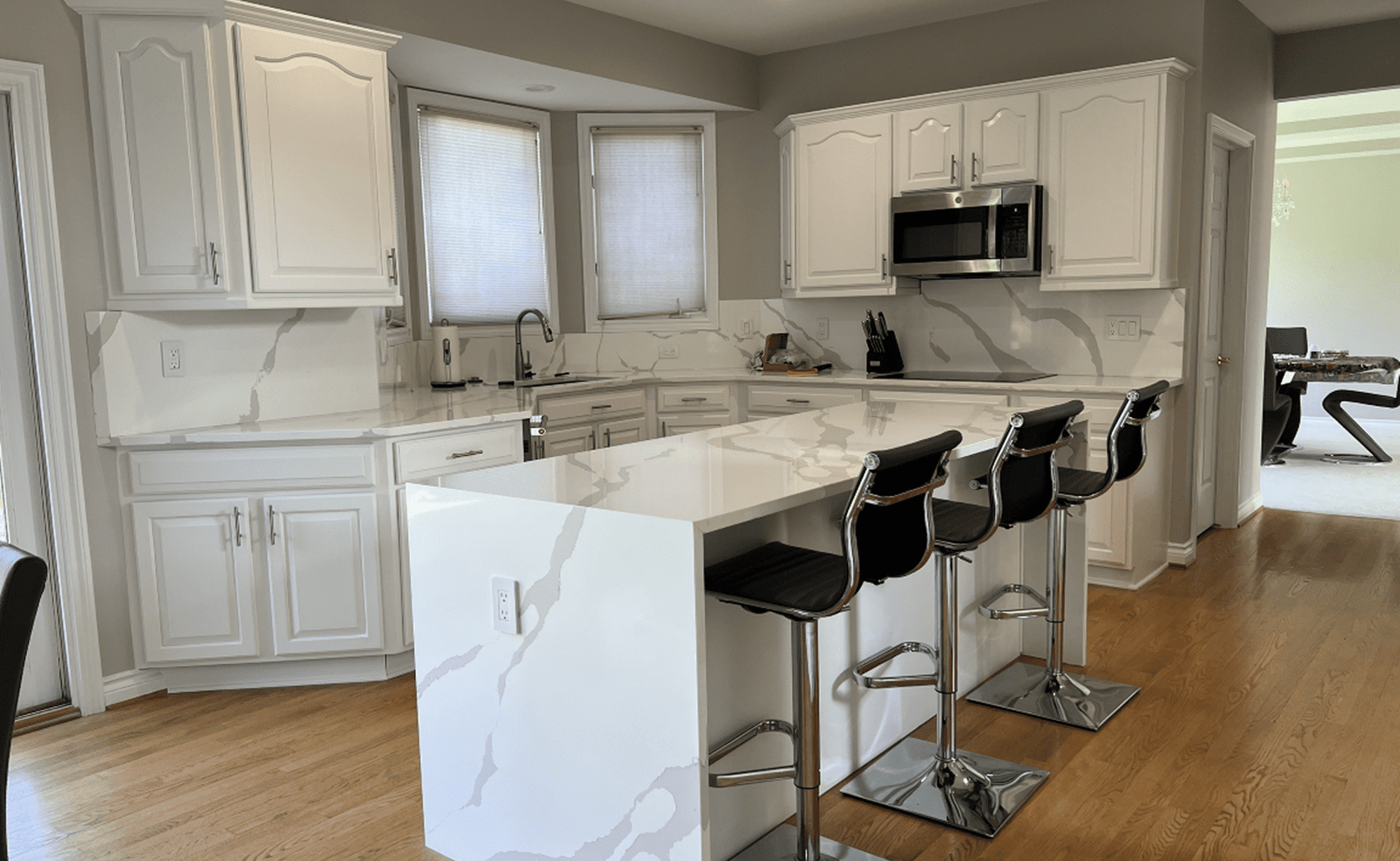 Modern kitchen with white marble island, black bar stools, white cabinets, and stainless appliances.