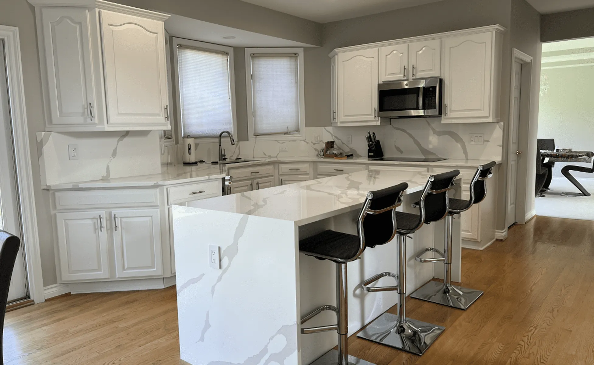 Modern kitchen with white marble island, black bar stools, white cabinets, and stainless appliances.