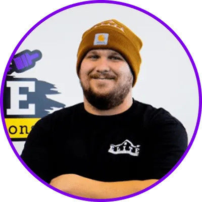 A person in a brown beanie and black t-shirt with crossed arms, logo background visible.