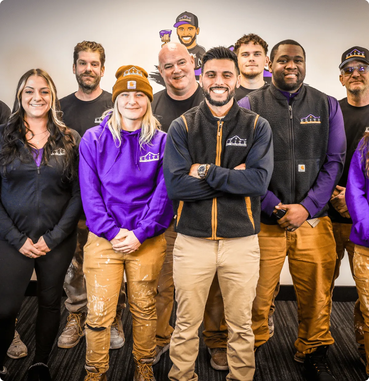 Nine people in matching work uniforms stand together by a wall with a logo.