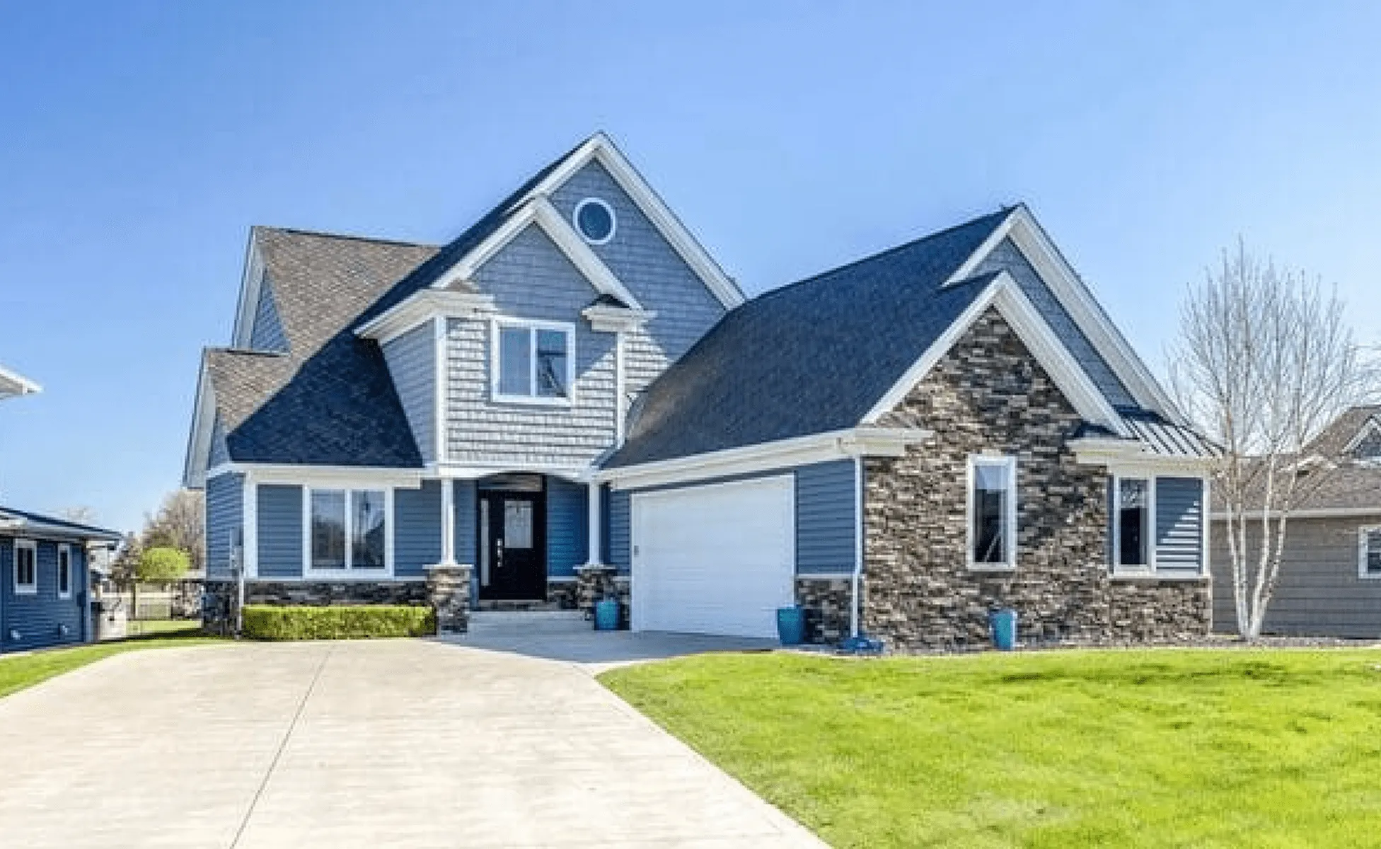 Two-story house with gable roof, stone and siding exterior, driveway, and green yard under blue sky.